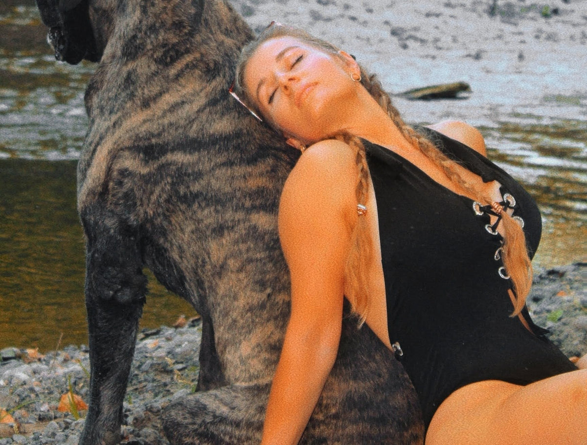 woman with black one piece swimsuit leaning on a big dog