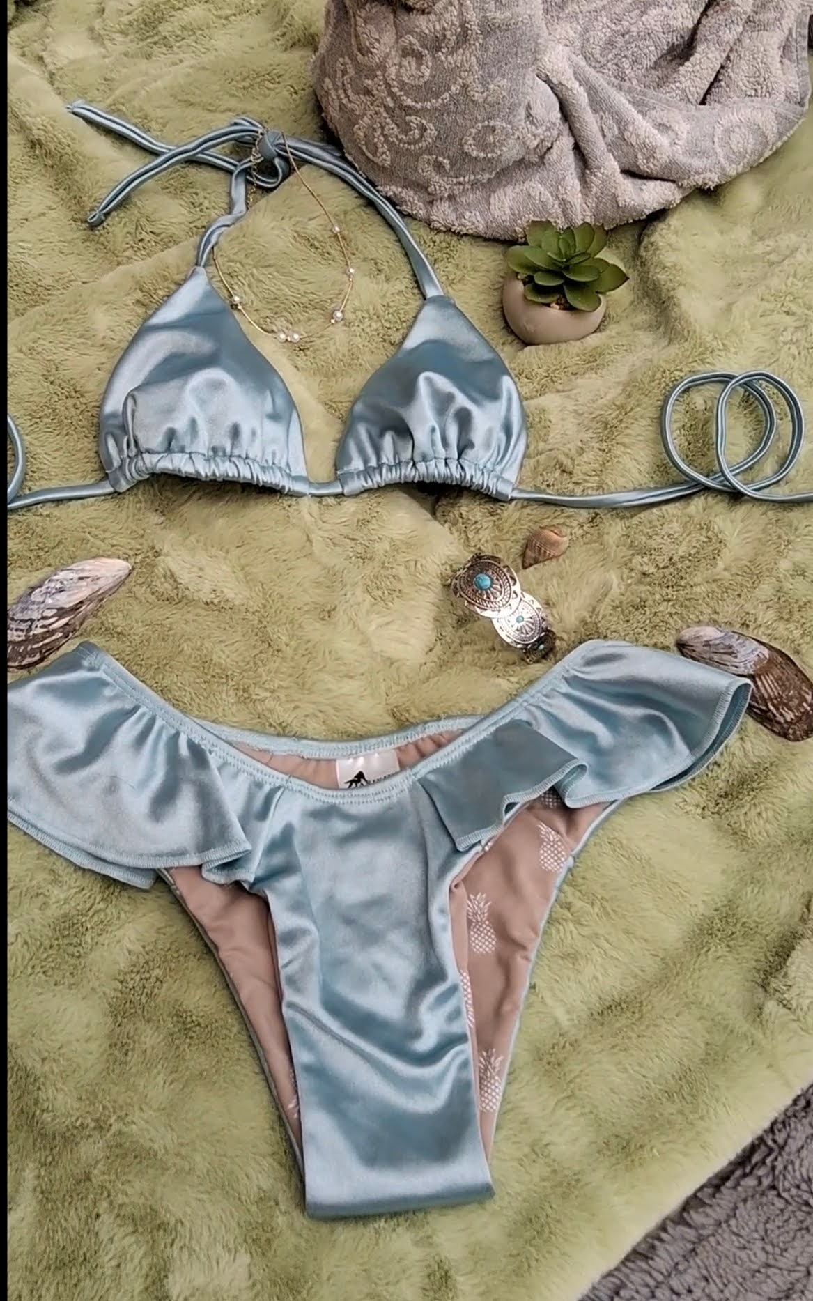Silver blue bikini set on a sandy surface with pebbles and a towel - Jasikini swimwear.