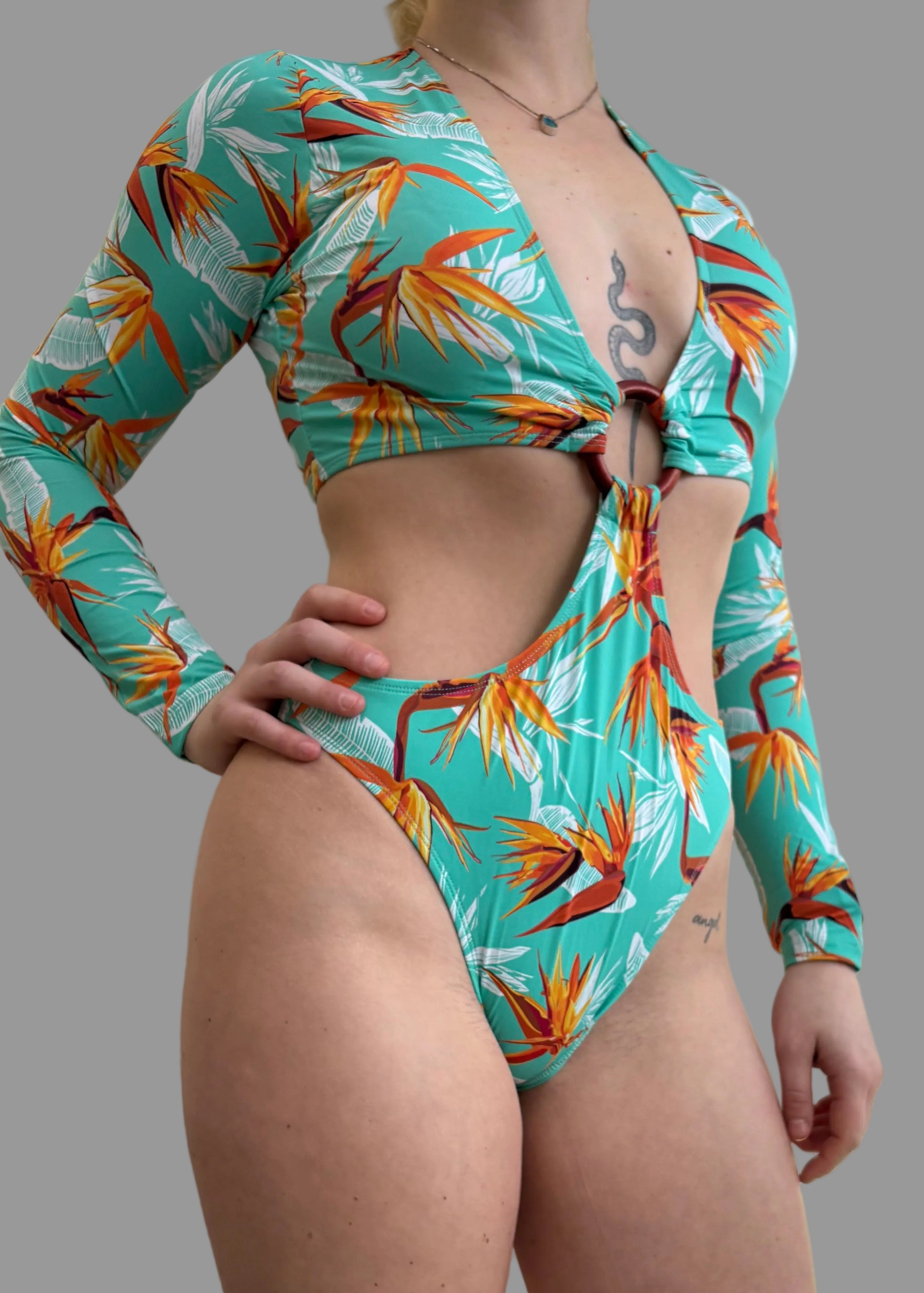 Woman wearing a turquoise long arm, one - piece swimsuit with floral pattern - Jasikini swimwear
